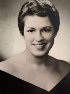 A vintage, black-and-white photo of a woman with short hair and an off-the-shoulder dress.