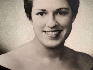 A vintage, black-and-white photo of a woman with short hair and an off-the-shoulder dress.